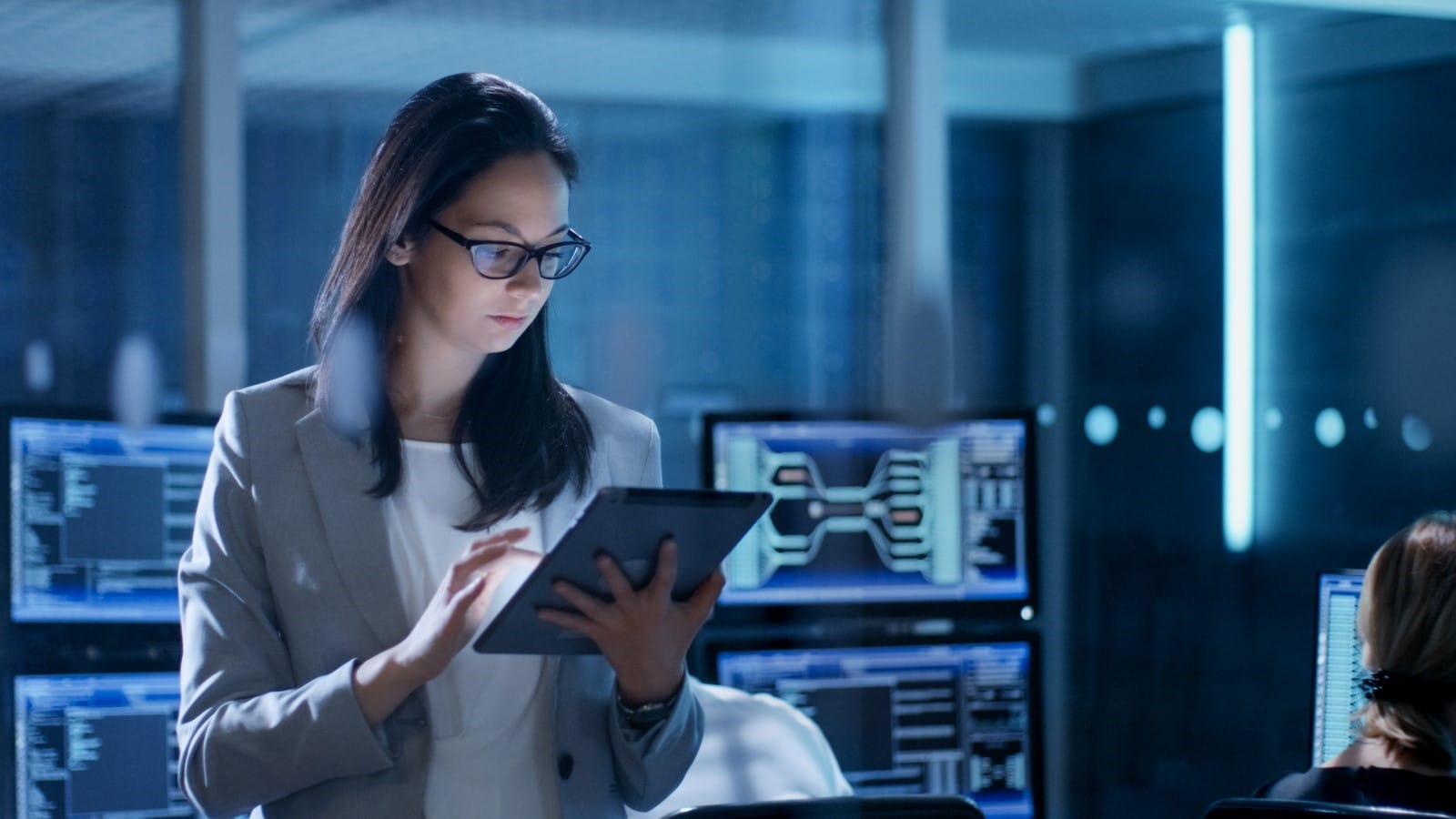A businesswoman looks down at a tablet held in her hand.