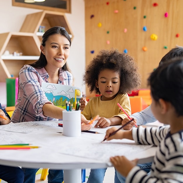 A female teacher helps three young students on their art projects