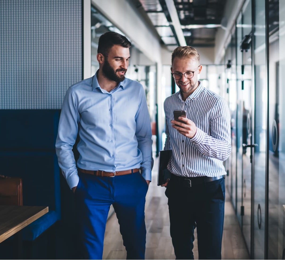 A photo of two men talking and walking down an office hallway.