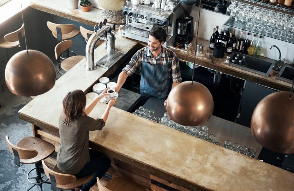 An employee hands a cup of coffee to a woman across a bar at a restaurant.