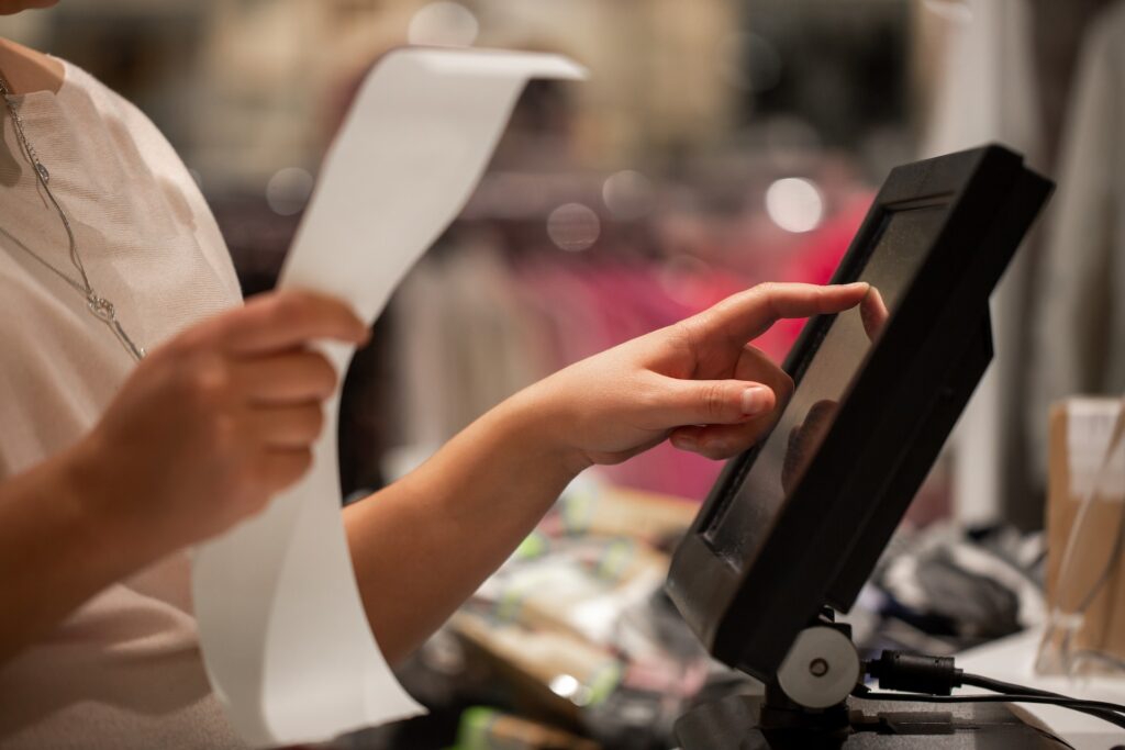 A person holding a receipt taps on a point-of-sale monitor.