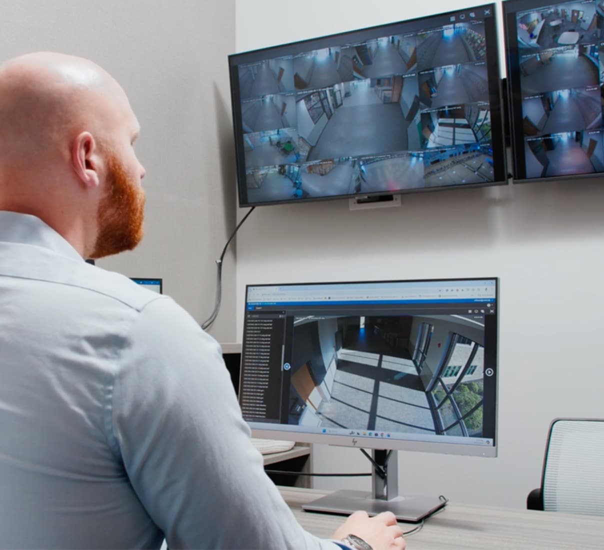 A security guard monitors three screens of security footage while seated at a desk