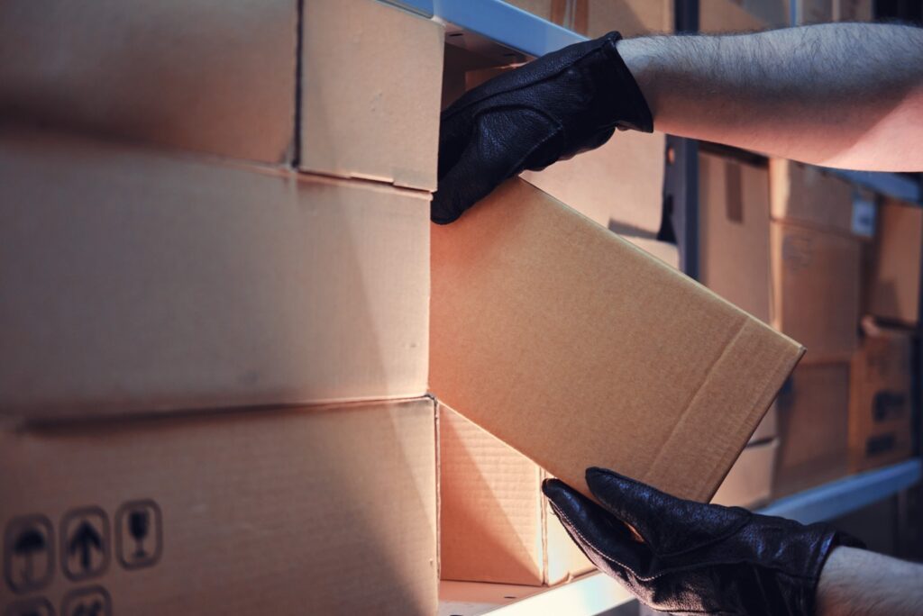 A person in black gloves carefully removes a cardboard box from a stack of boxes