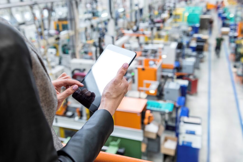 A woman utilizes a tablet in an industrial factory setting, surrounded by various machines and production equipment.
