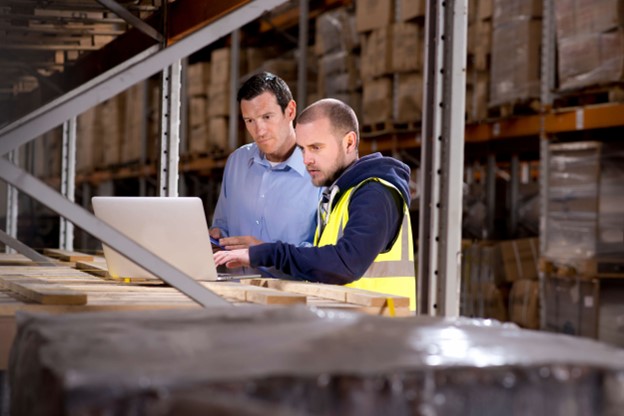 Two men collaborate on a laptop inside a spacious warehouse