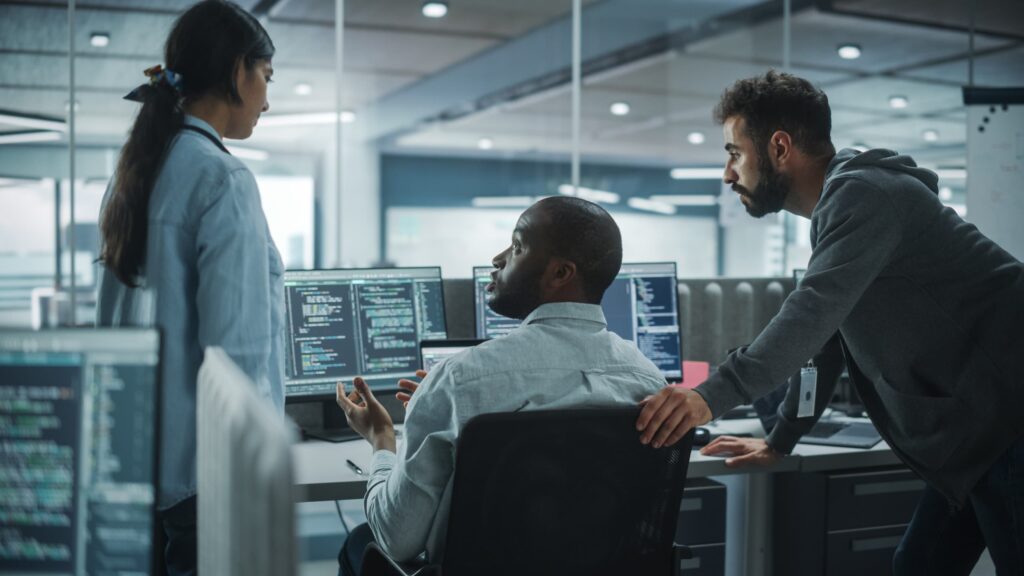 Three people huddle together in front a computer monitor