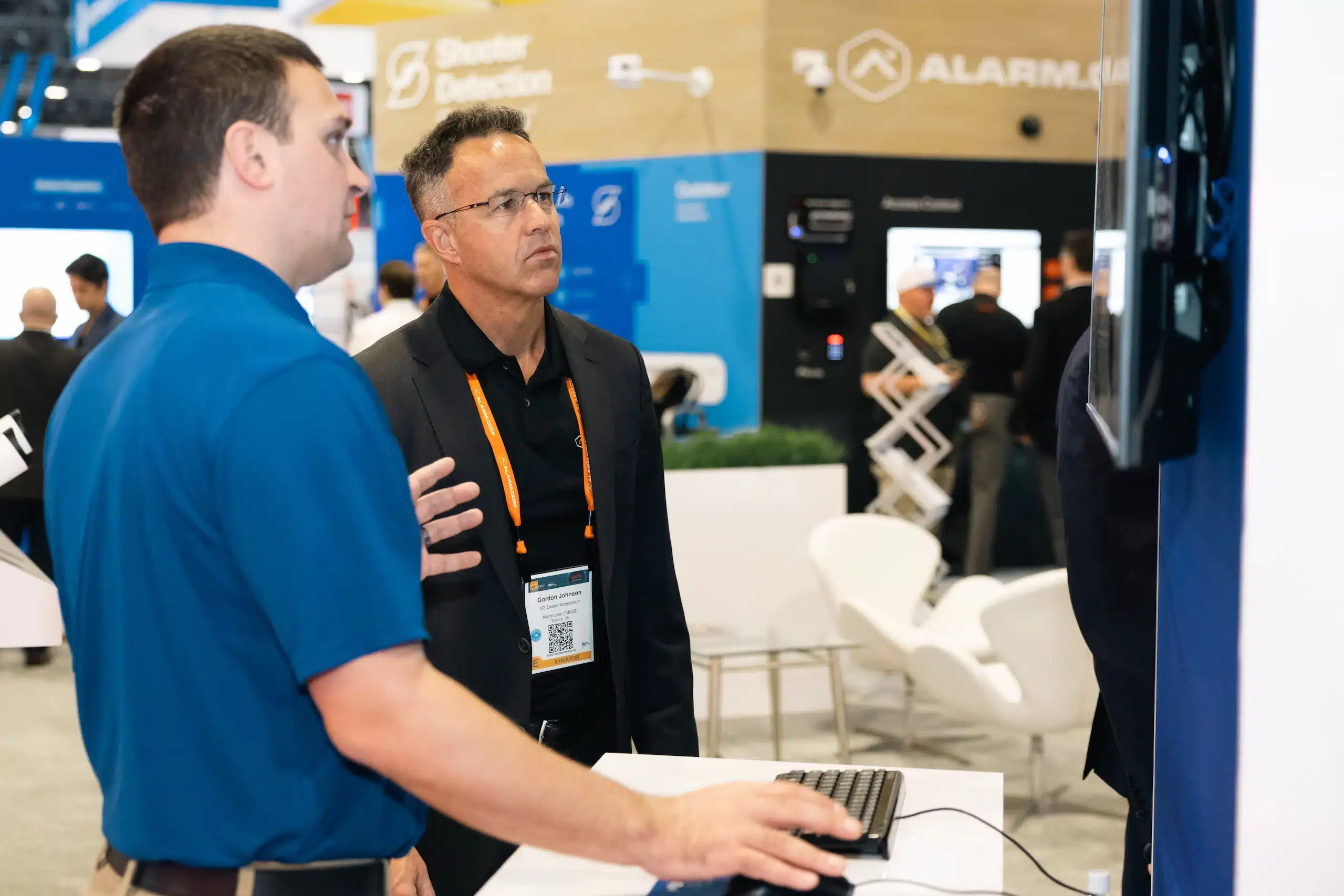 Two men stand in front of a monitor at an OpenEye trade show booth