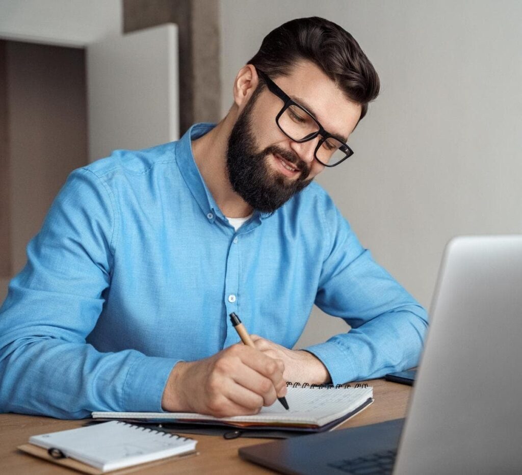 Man taking notes in front of laptop