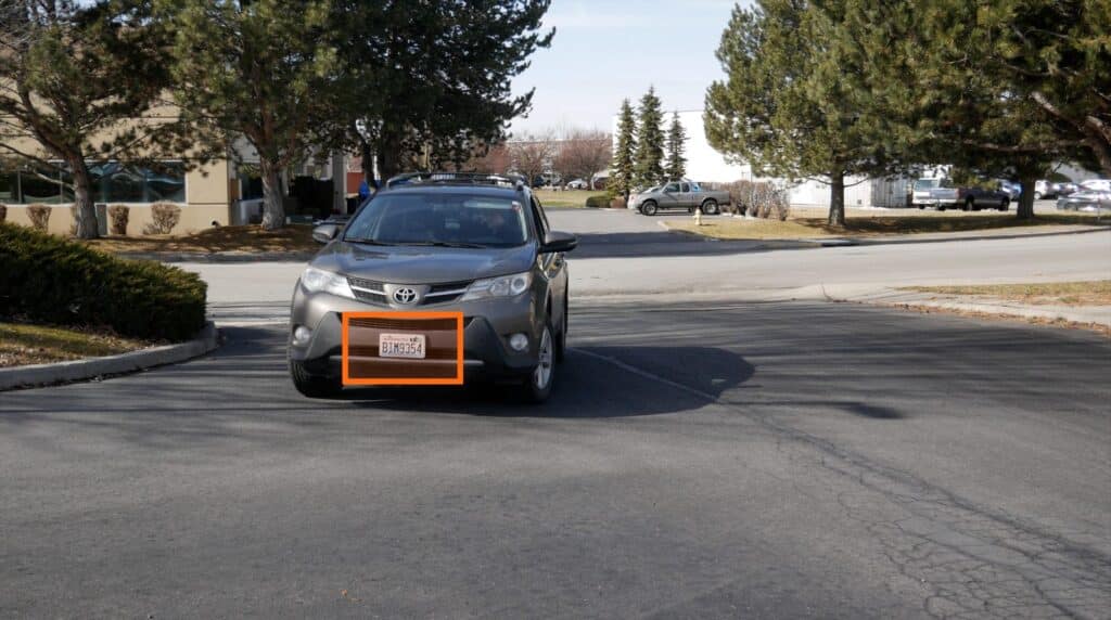 A vehicle entering a parking lot with a license plate recognition alert visible on the plate.