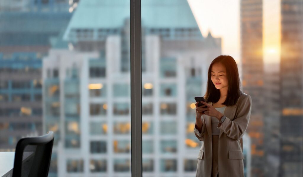 A woman stands in an office, looking at her phone