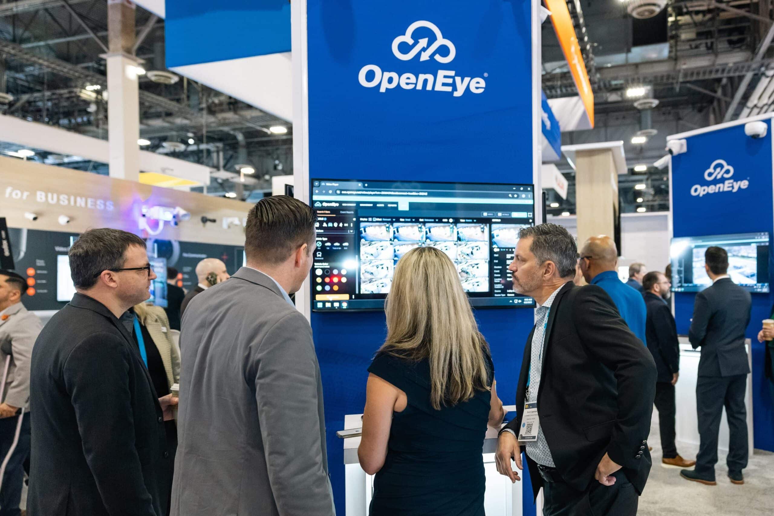 A group of four people gathered in front of an OpenEye kiosk on a trade show floor