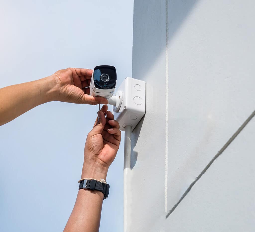 A person positions a video surveillance camera against an exterior wall