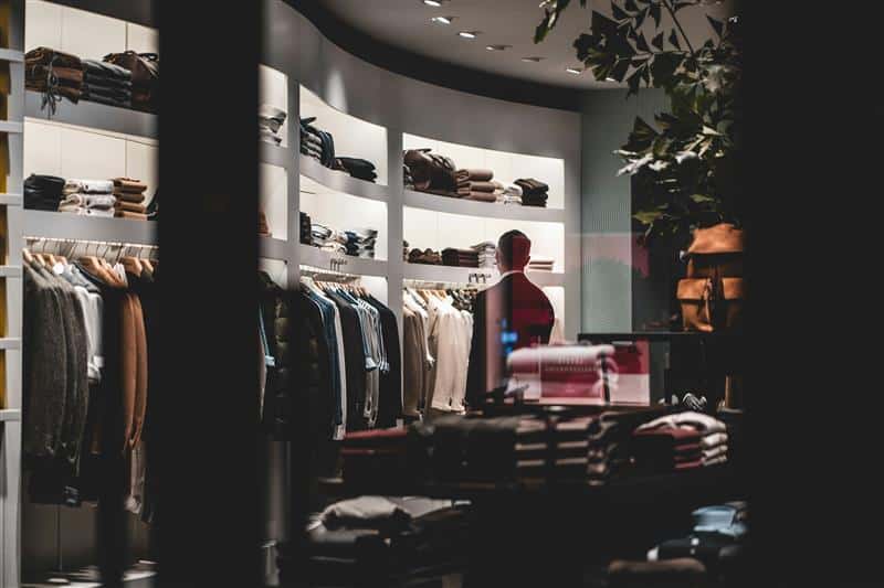 A man stands inside a luxury retail store, surrounded by racks of clothing and accessories