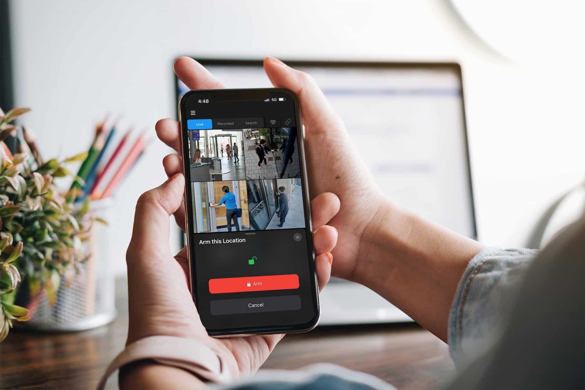 A person holding a mobile phone that displays four camera feeds in OWS with a prompt to arm the location