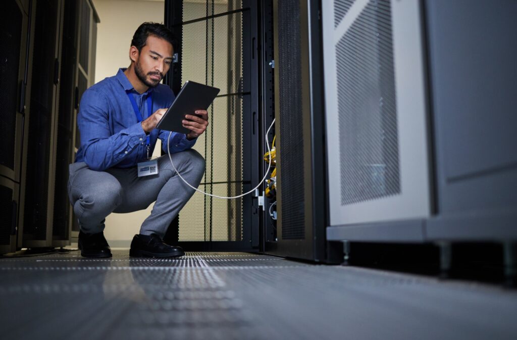 A man kneels in front of a server, focused on troubleshooting or maintaining the equipment