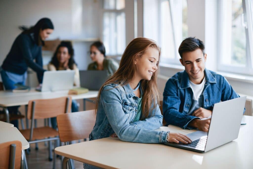 Two students work together on a laptop in a classroom