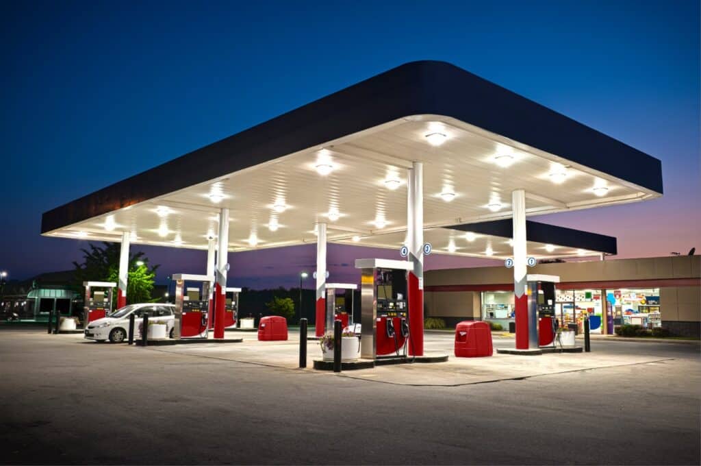 A gas station illuminated at night, with several cars parked in front under the bright lights.