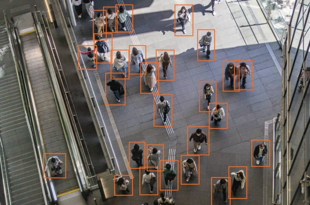 A group of people waiting on a train platform surrounded by orange bounding boxes