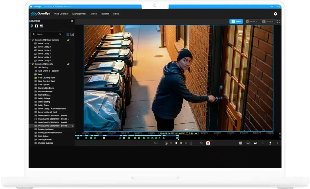 A laptop and phone feature video of a man standing in an alleyway, looking towards the camera while trying to enter a building