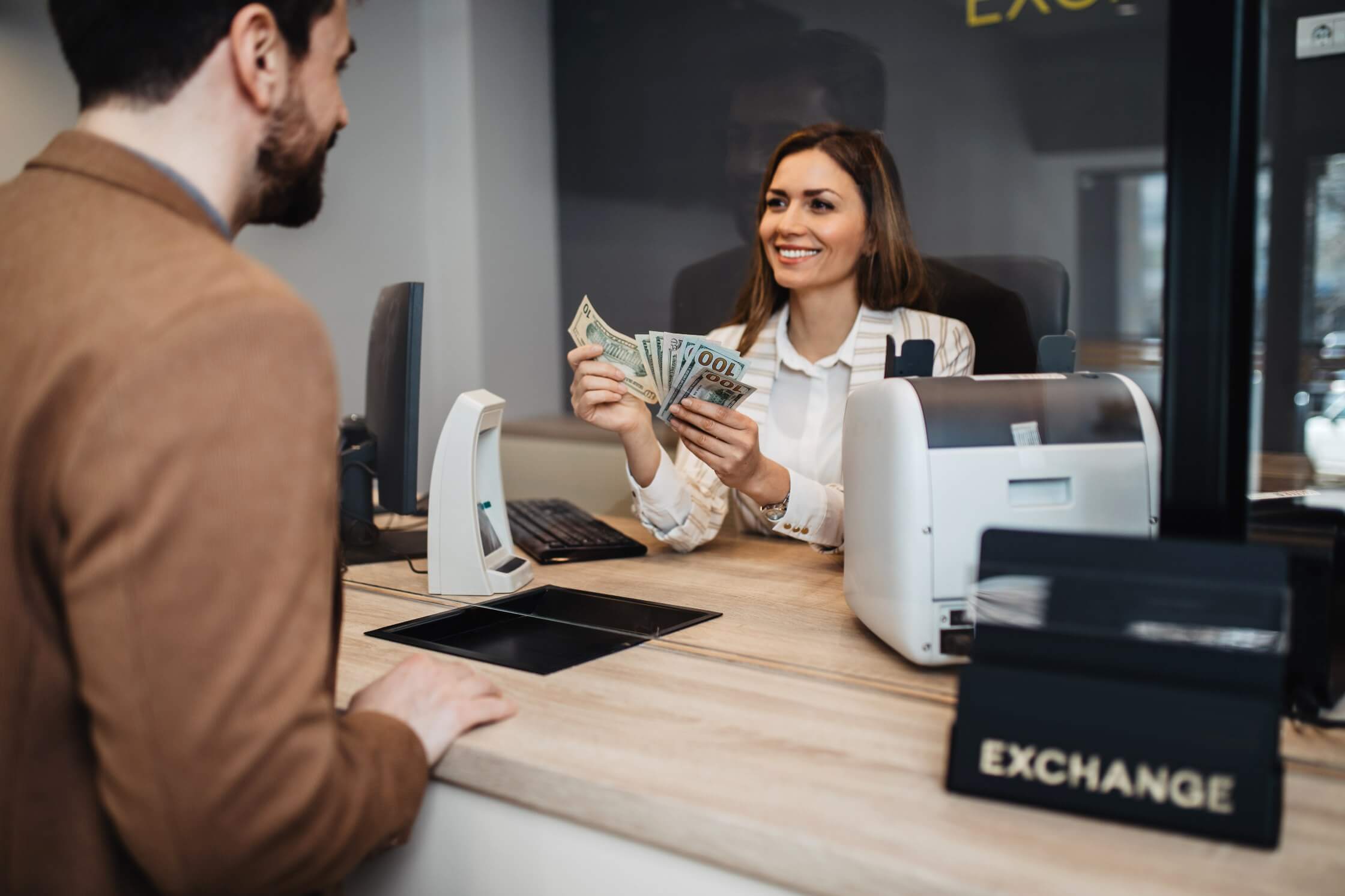 A female bank teller counts cash while assisting a male customer