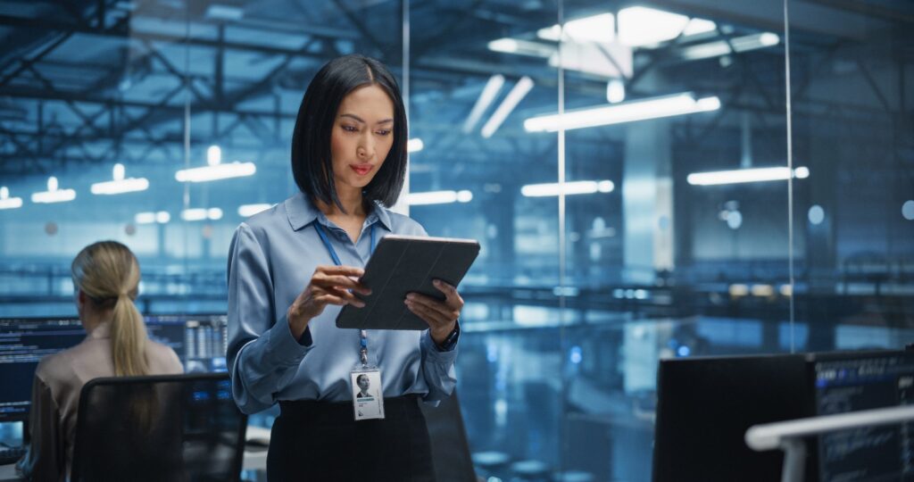 A woman in a business suit holds a tablet in a professional setting.