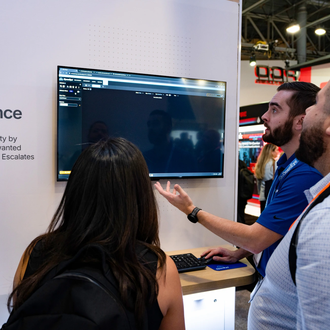 An OpenEye employee gives a demo to two people in a trade show booth