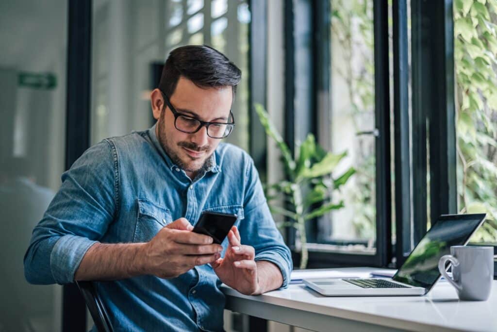 A man wearing glasses stares down at his phone