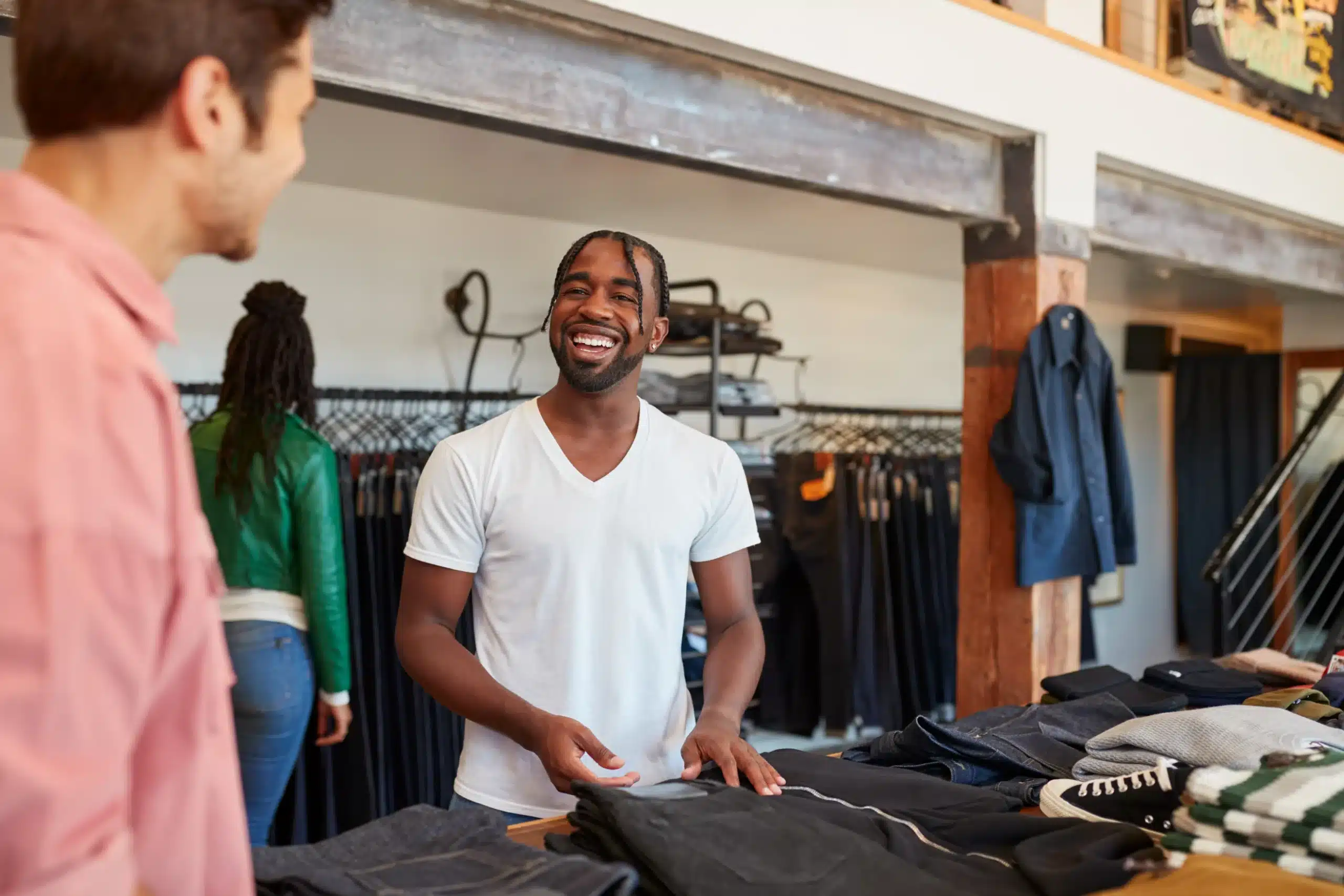 Two men engage in conversation while browsing clothing in a retail store.