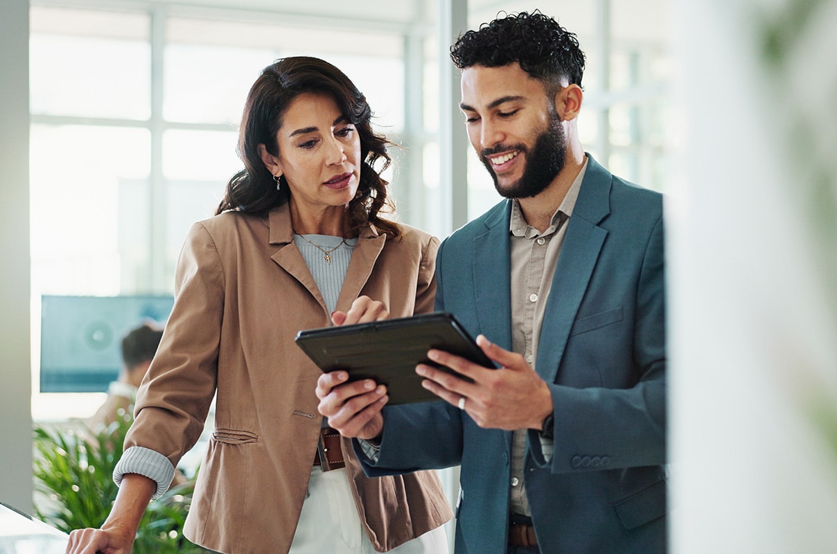 A man and woman in business attire are collaborating while looking at a tablet together.