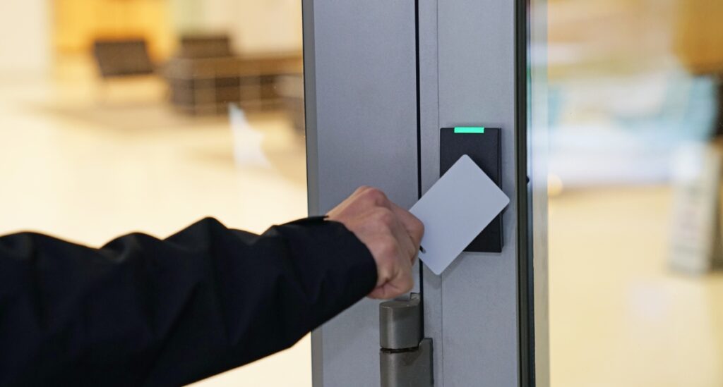 Hand holding key card to access control panel on glass door.