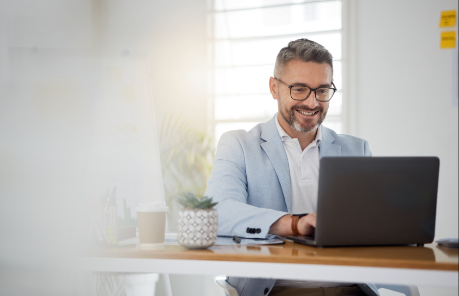 Man sits in office setting smiling at laptop.