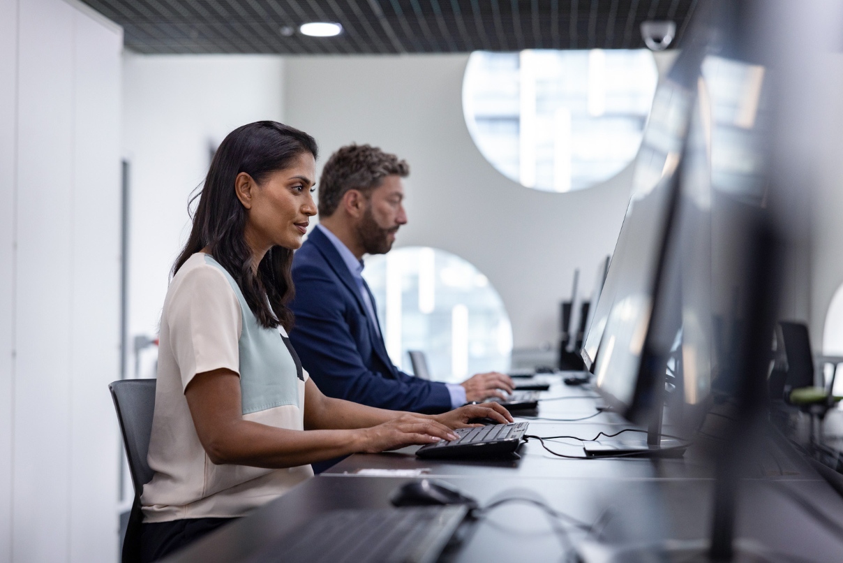 A man and woman sitting at desks looking at computers in a bank office setting.