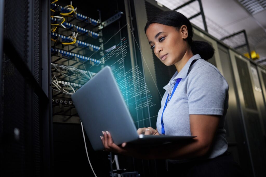 Woman standing near servers looking at laptop screen.