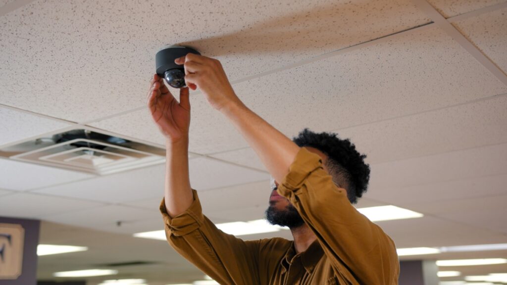 Man reaching up to a dome security camera attached to an office ceiling.