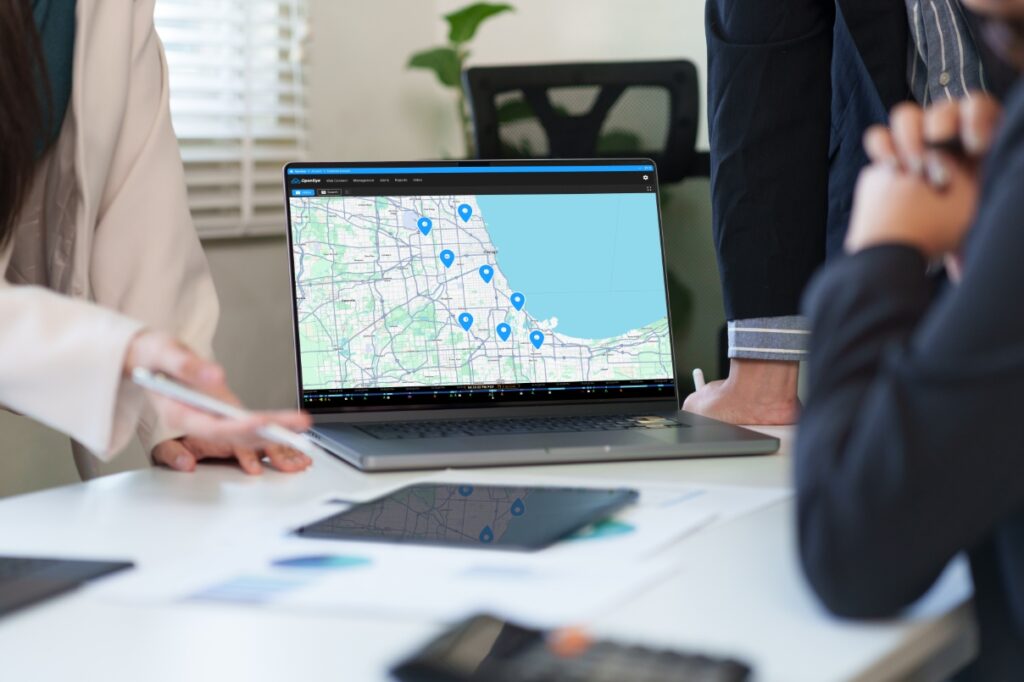 Person in office setting pointing to computer displaying OpenEye Web Services with other people around.