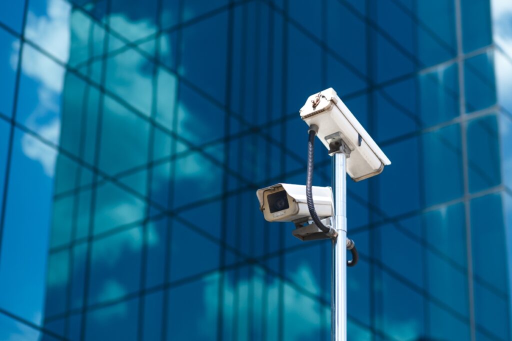 Two security cameras face opposite directions in a city setting.