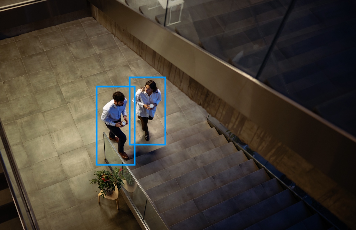 Two people walk in a building surrounded by bounding boxes created by AI-powered video surveillance.