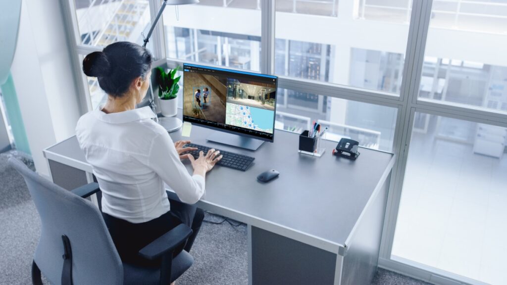 Woman in an office looks at computer which displays OpenEye Web Services live video security feeds.