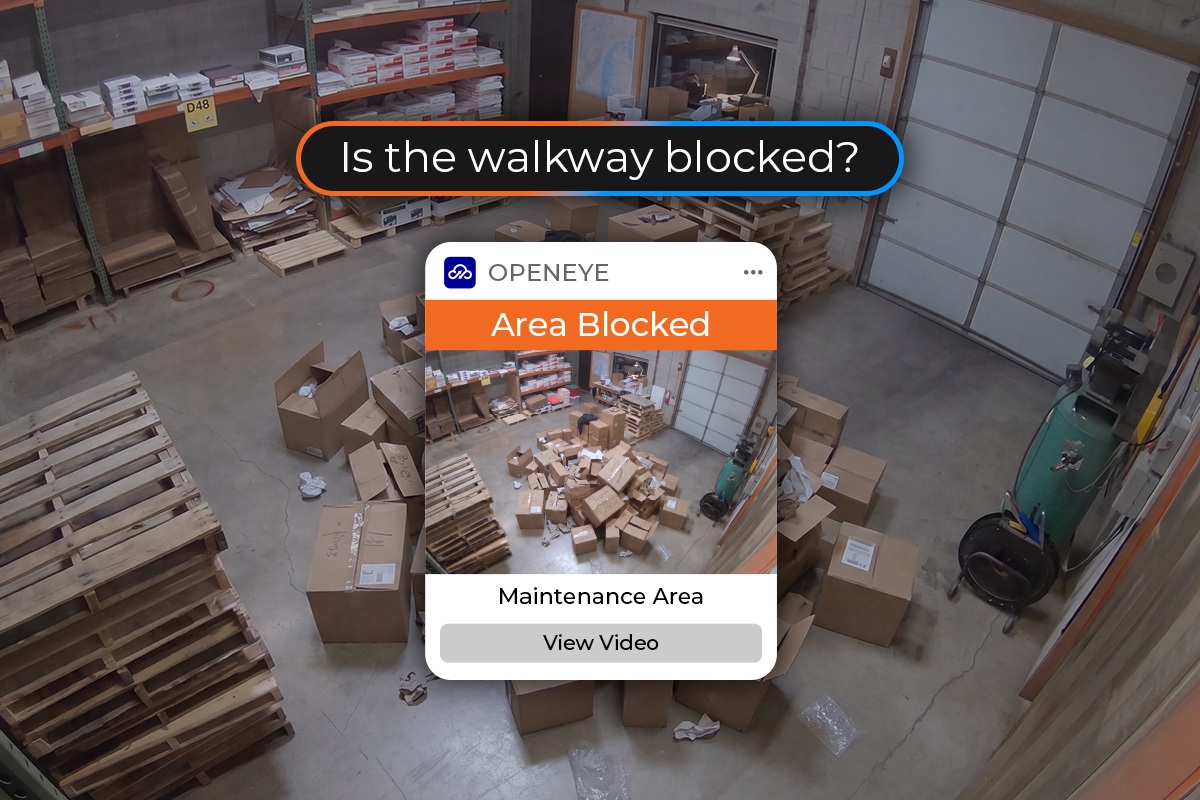 A warehouse scene depicts a pile of boxes blocking the center of a room, with a prompting screen and alert in the middle of the scene reading, "Is the walkway blocked? OPENEYE. Area Blocked. Maintenance Area. View Video."