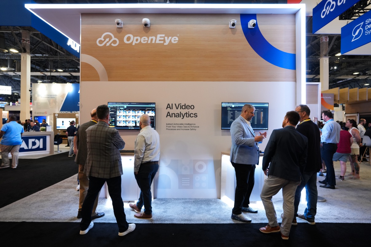 A group of people stand at OpenEye's booth during a physical security event.