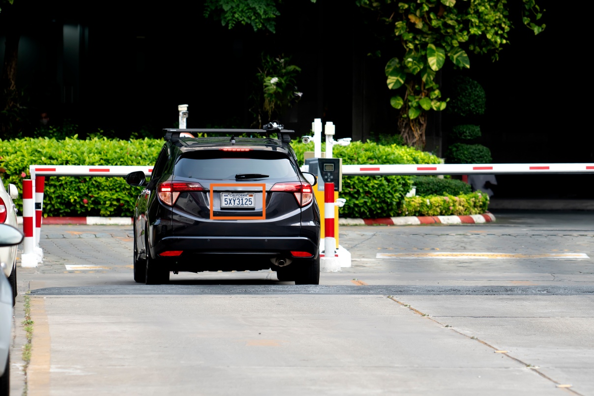 A black car waits behind a parking gate arm with a bounding box shown around the car's license plate, signifying the use of license plate recognition technology.