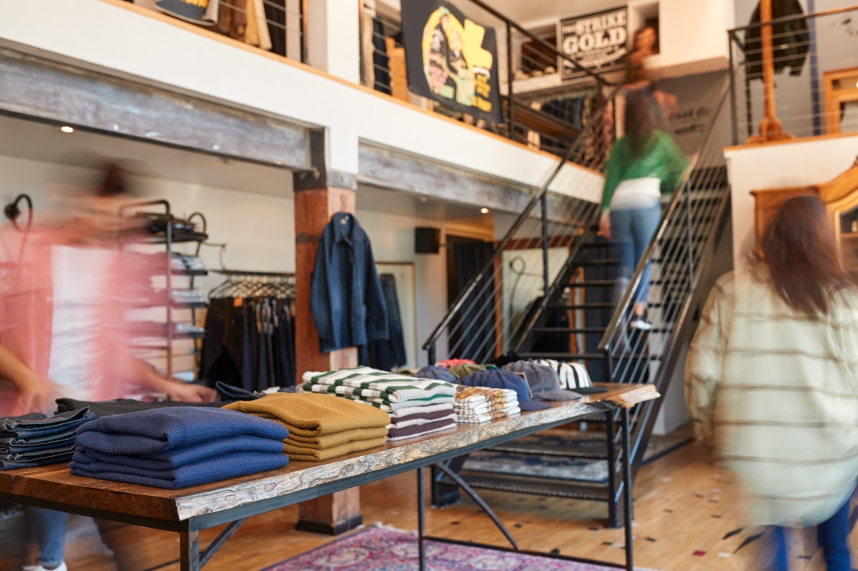 Multiple people navigate a busy retail clothing store.