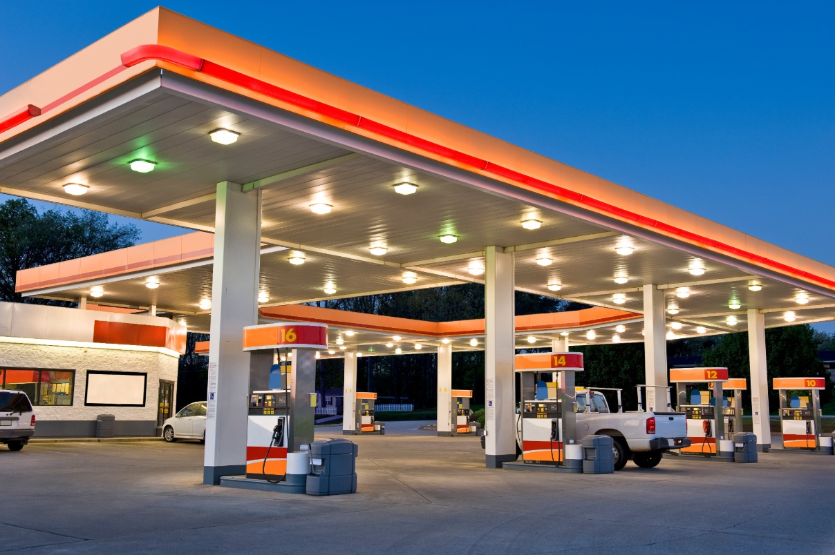 Multiple cars are parked at gas pumps or in front of a gas station at night.